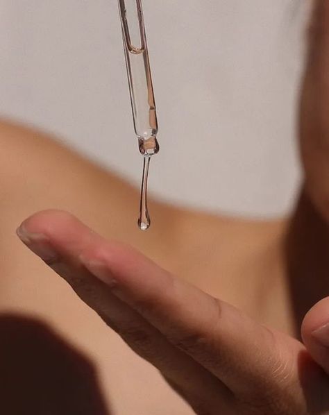 Clear Korean skincare serum being dropped into a clean hand using a glass dropper